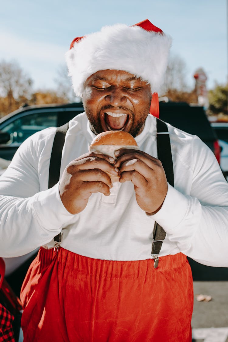 A Man In A Santa Costume Biting A Burger