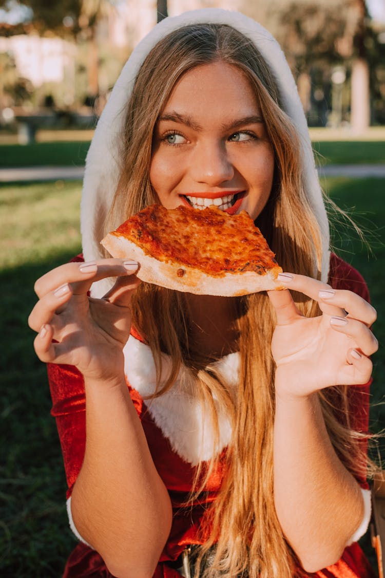 Woman In Santa Costume Biting A Slice Of Pizza