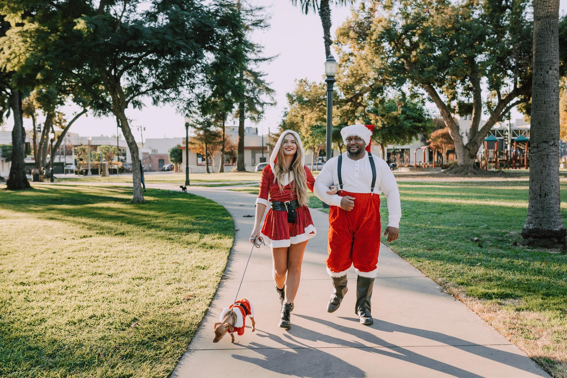 Man And Woman In Santa Outfit Walking On Concrete Pathway With A Dog