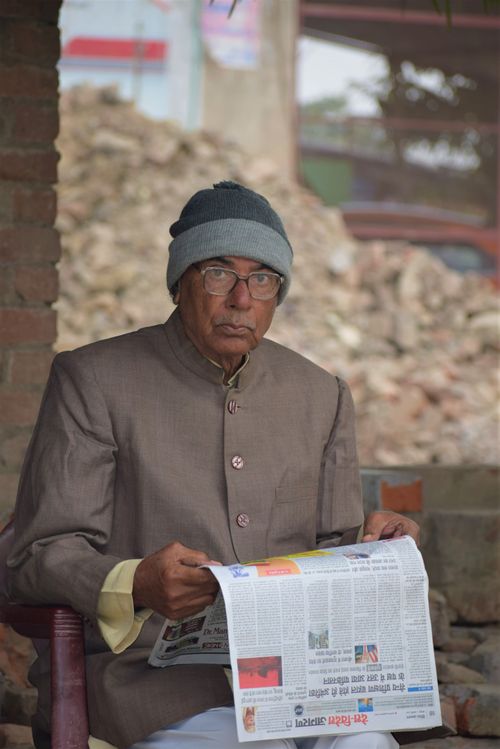 Free Elderly Indian man with glasses and beanie reading a newspaper outdoors in Kanpur. Stock Photo