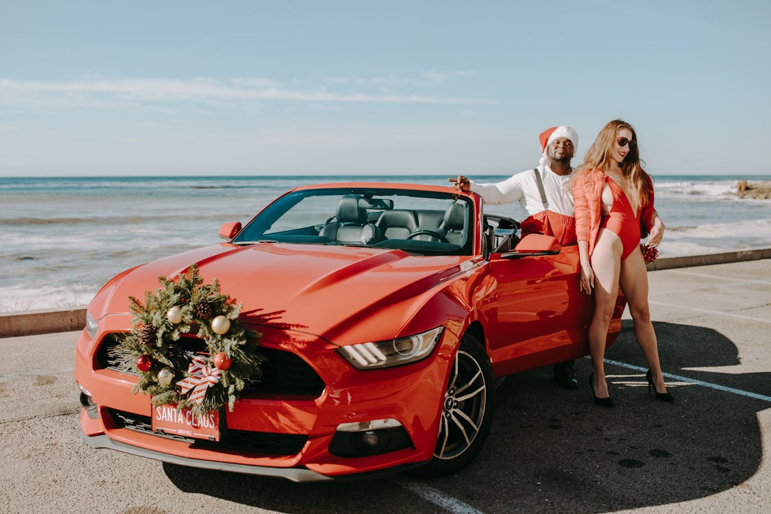 Meestal escaleren Grace Man In Santa Outfit En Sexy Vrouw Naast Rode Auto · Gratis stockfoto