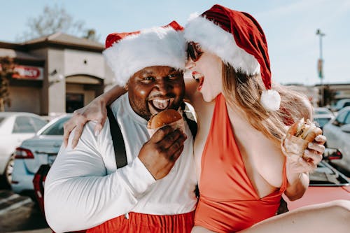 Man And Woman In Santa Outfits Eating Hamburger Sandwiches