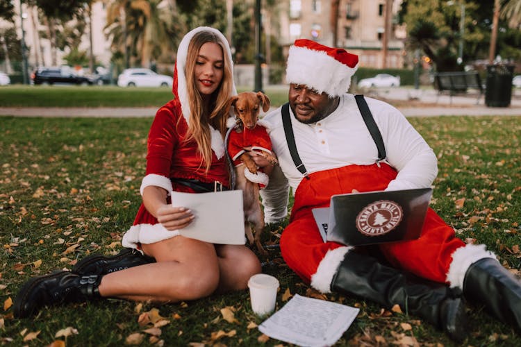 People And Dog In Santa Costume Sitting In The Park