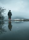 Man in Black Jacket Standing on Snow Covered Ground Near Body of Water