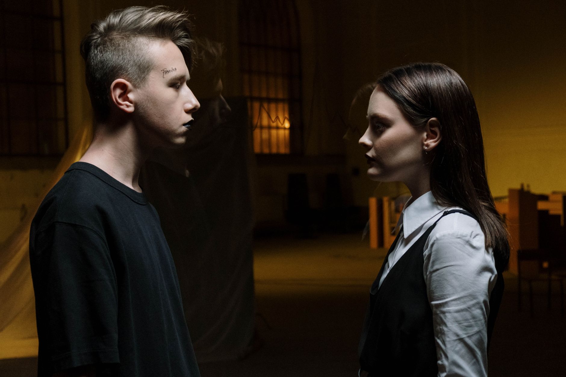 Two young adults facing each other intensely in dim lighting indoors. Two young adults facing each other intensely in dim lighting indoors.