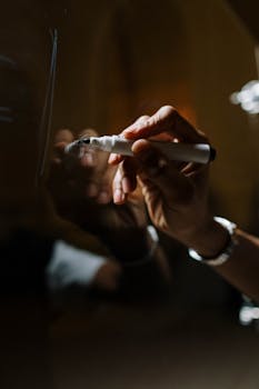 A close-up of a hand writing with a marker on a glass board, capturing reflections and details.