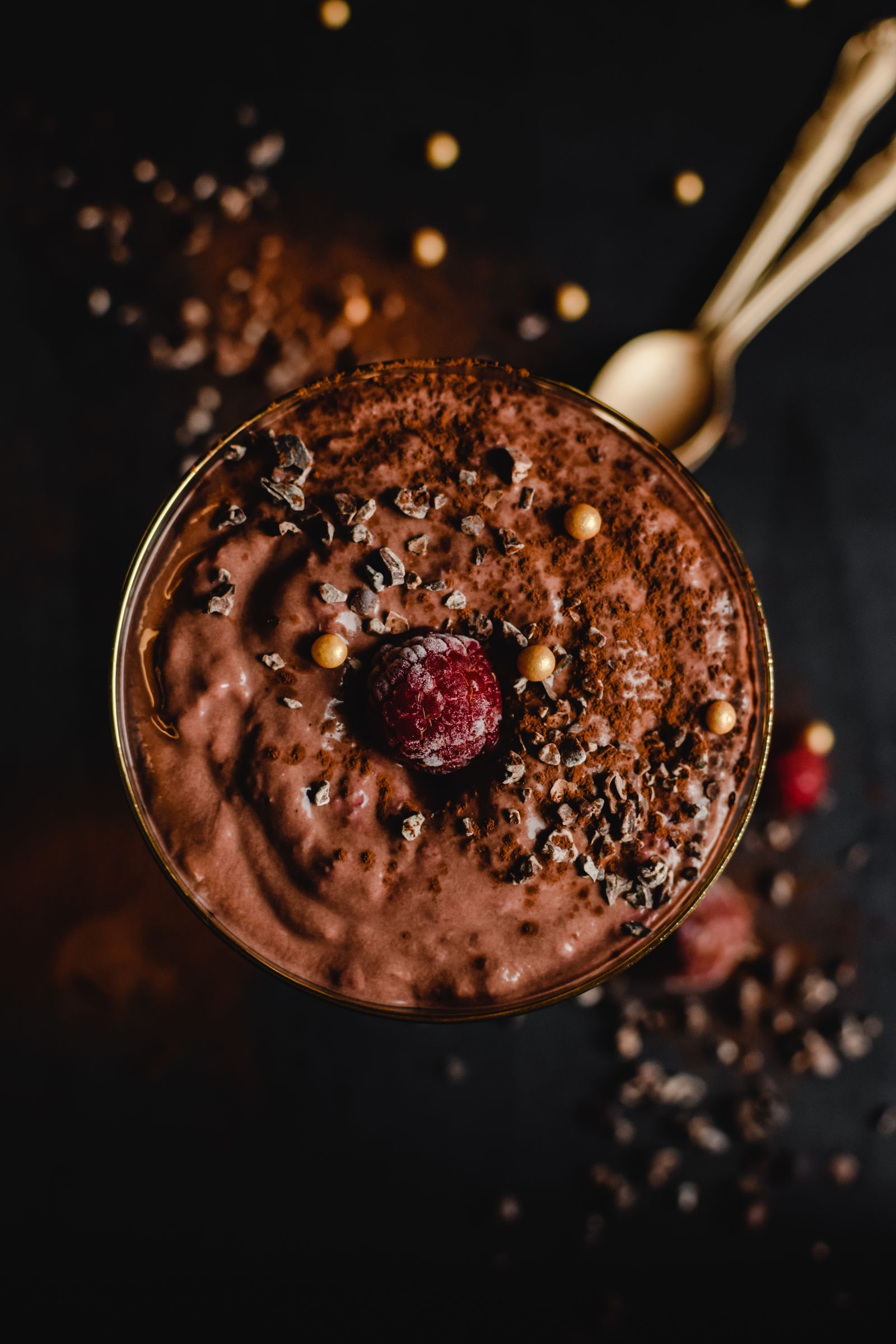 Chocolademousse met framboos en gouden parels op een donkere achtergrond.