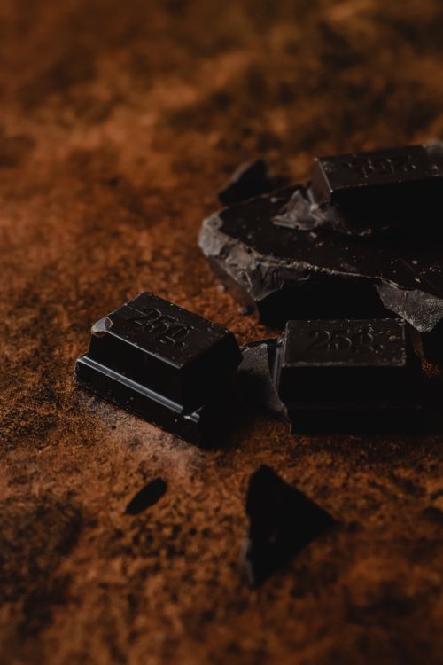Free Close-up of dark chocolate pieces on cocoa powder background, showcasing rich texture and color. Stock Photo