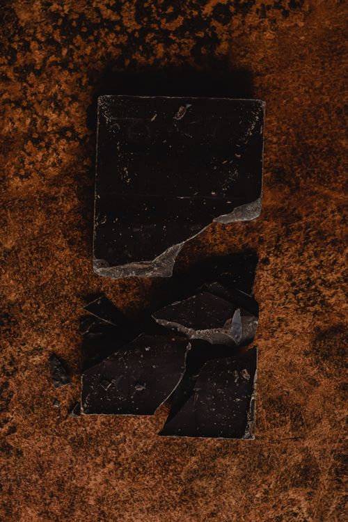 Free Close-up of broken dark chocolate on a textured brown surface. Ideal for dessert themes. Stock Photo