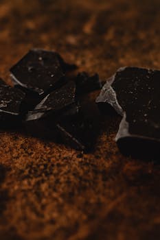 Dark chocolate chunks scattered on a rustic surface, captured in a warm, close-up shot.