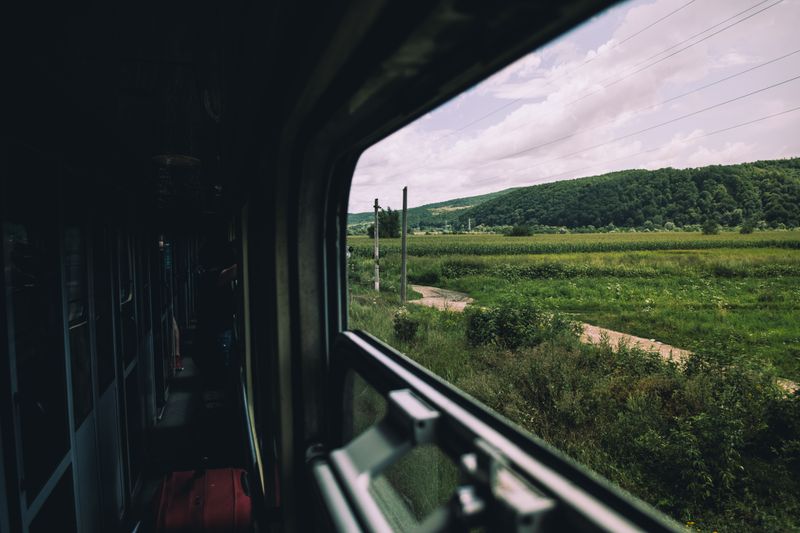 Scenic view of green countryside and hills from a moving train window during summer.