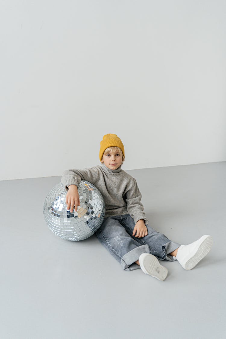 A Boy Wearing A Bonnet And Sitting Next To A Disco Ball