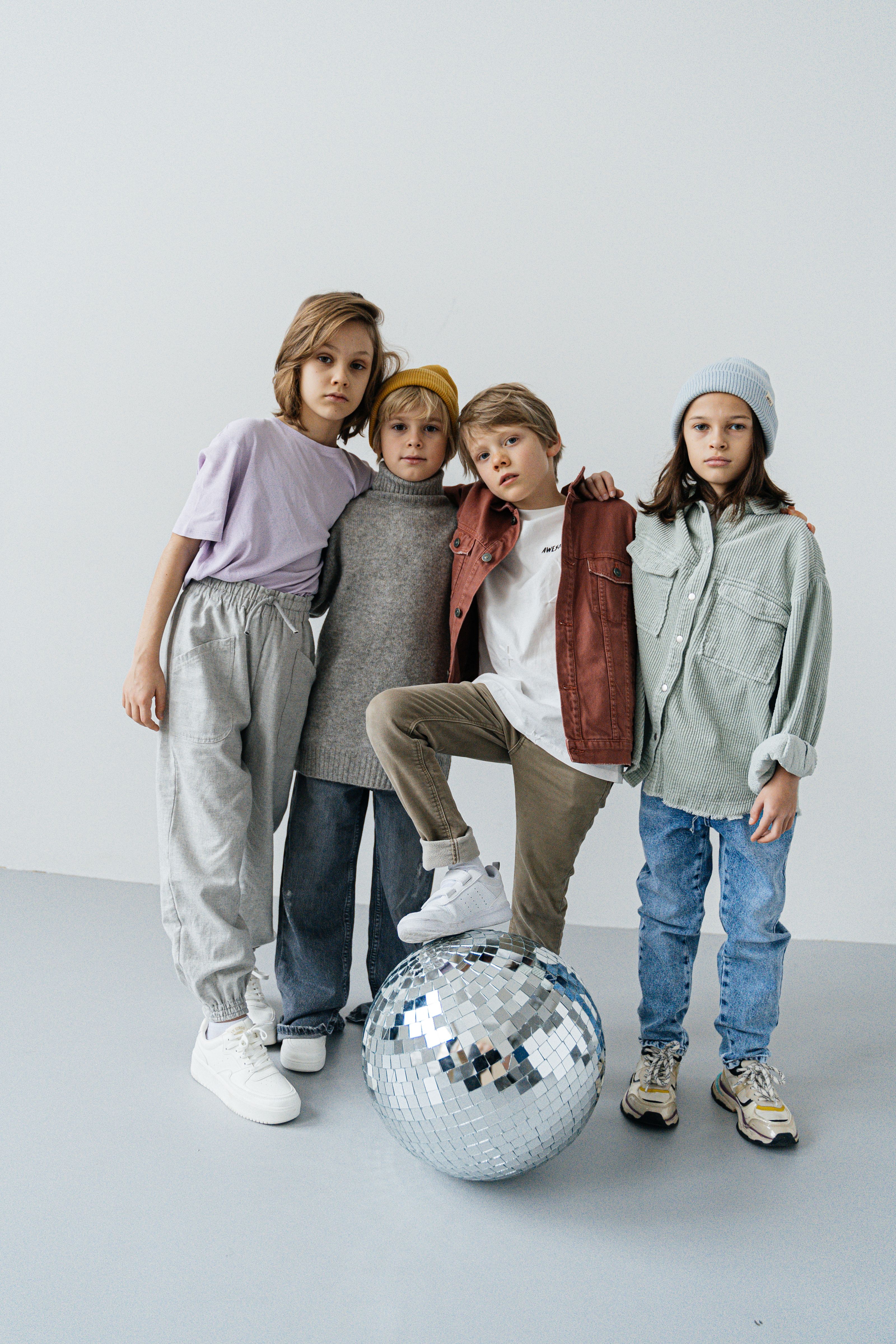 Crianças vestidas à moda posam com uma bola de disco, exibindo estilo moderno.