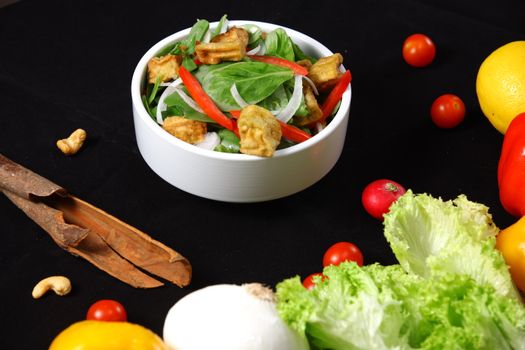 A vibrant vegetable salad with lettuce, peppers, and tofu in a white bowl on a black background.