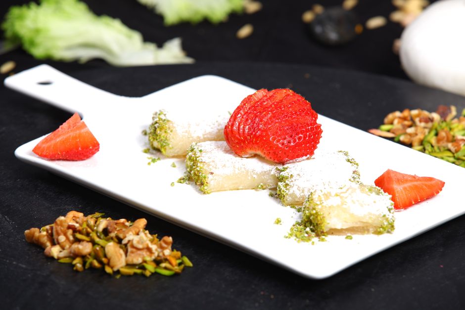 Chocolate-dipped strawberries coated in golden toasted shredded phyllo and crushed pistachios, arranged on parchment paper with a pistachio cream drizzle.