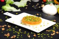 Delicious Middle Eastern Kunafa dessert garnished with pistachios on a white plate, surrounded by fresh ingredients.