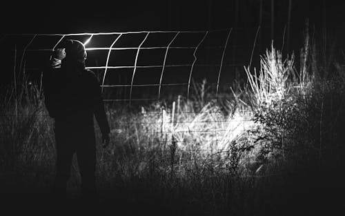 Grayscale Photo of Man Standing Near Fence