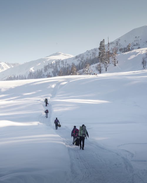 People with Backpacks Walking on Snow Covered Hill during Winter