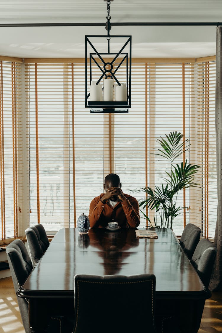 A Person Sitting At A Table With A Cup Praying