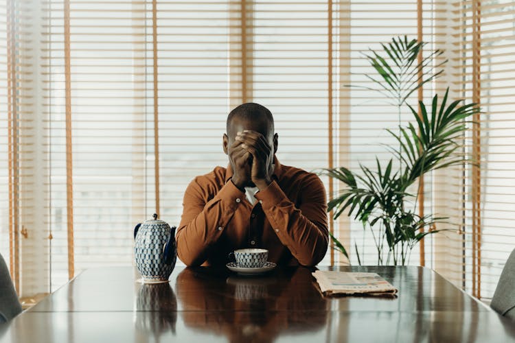 A Man Sitting At A Table With A Cup Praying
