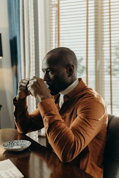 A man sitting indoors, enjoying a warm cup of tea by the window.