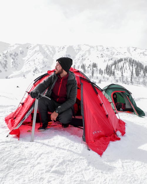 Miễn phí Người đàn ông Mặc áo Khoác đen Ngồi Trên Lều đỏ Trên Mặt đất Phủ đầy Tuyết Ảnh lưu trữ