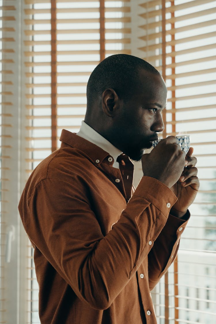 Man Drinking Tea Near Window Blinds