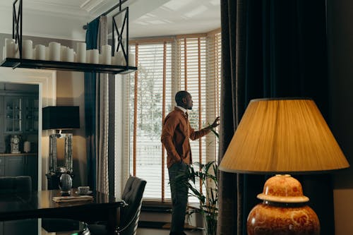 Man Standing Near the Window with Wooden Blinds