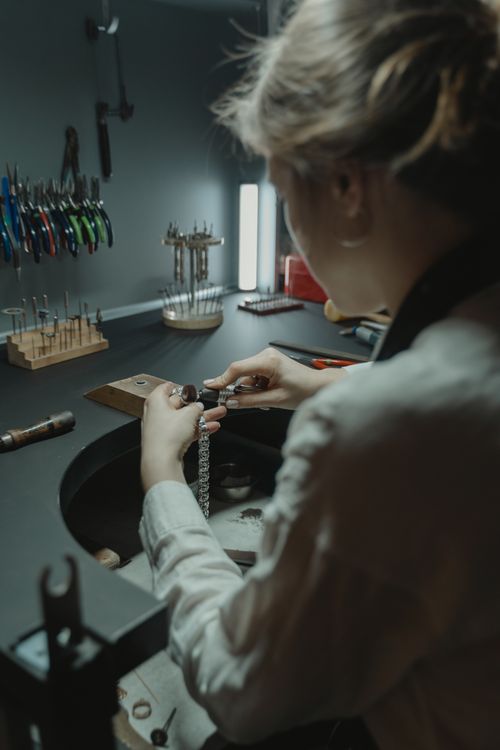 Free Jeweler working meticulously on necklace design at workbench in professional studio. Stock Photo