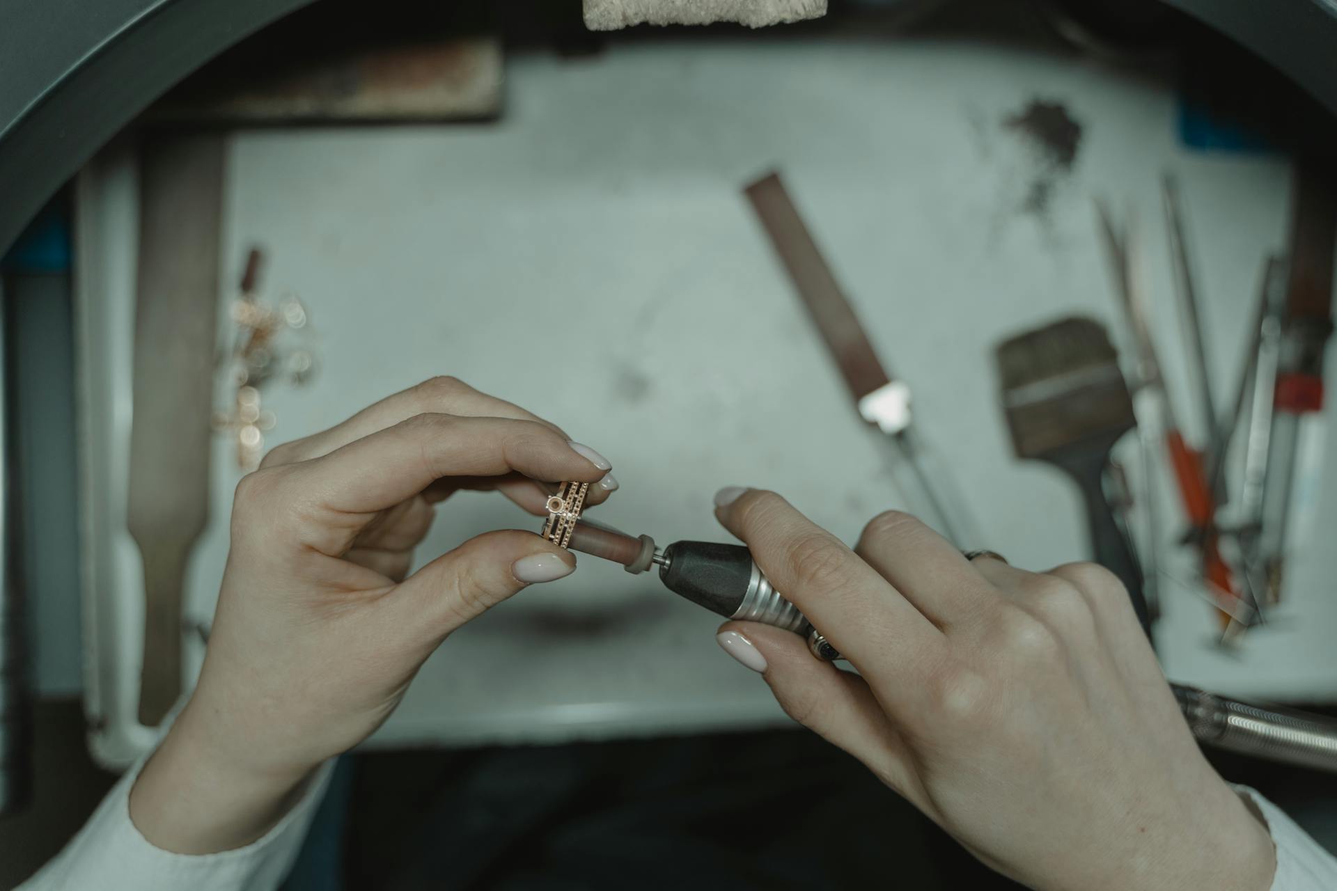 Close-up of hands using a rotary tool to polish a ring in a jewelry workshop.