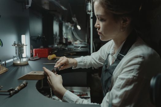 A skilled woman jeweler focusing on detailed craftsmanship in an indoor workshop.