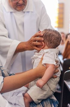 Elderly priest stroking baby during baptism ceremony