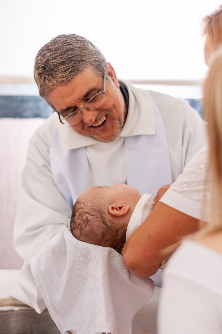 Smiling Priest Wiping Baby Head During Baptism Ceremony