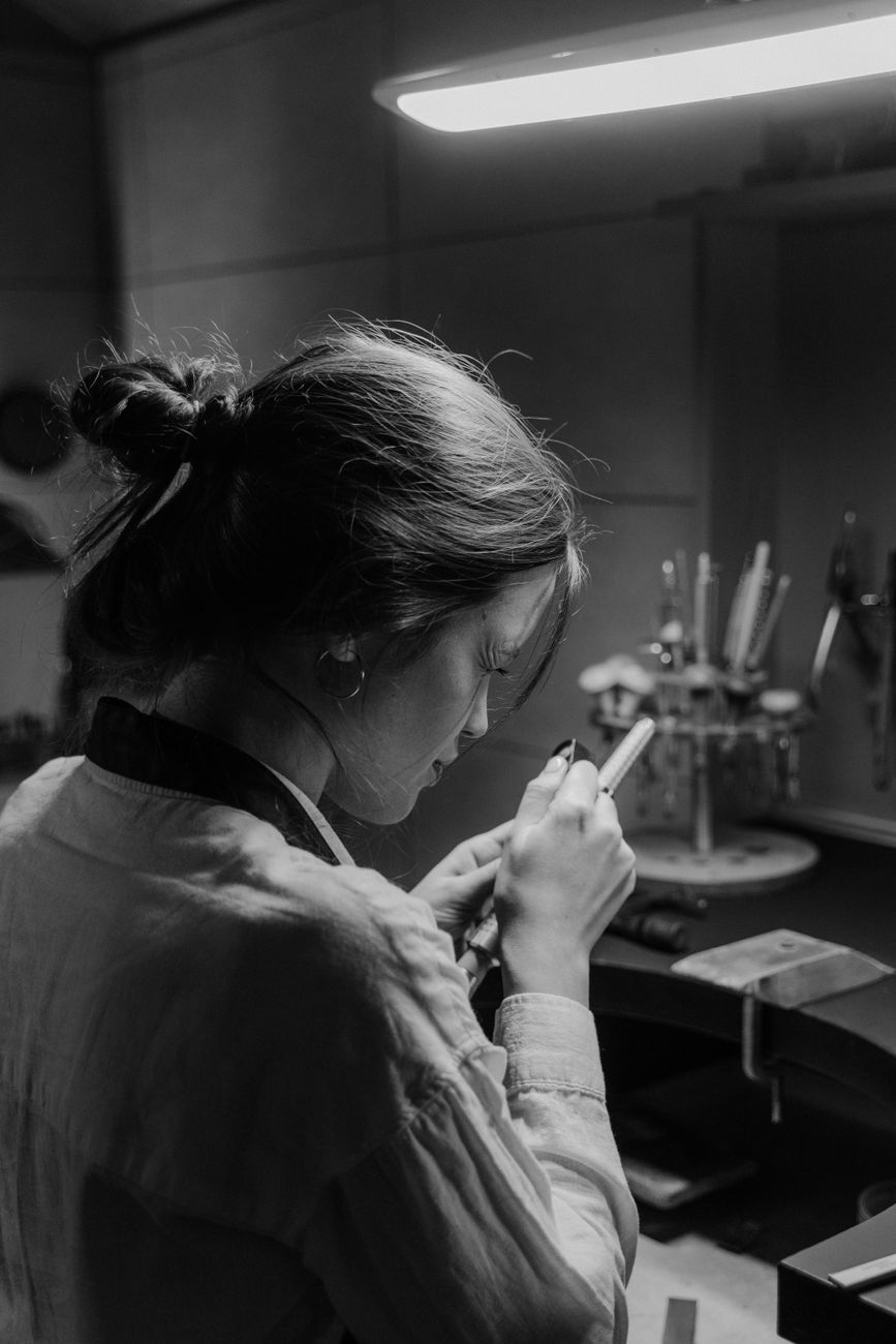 A focused female jeweler skillfully crafting in a monochrome workshop setting.