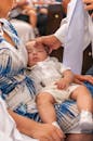 Priest touching head of adorable little baby sleeping on mother laps during baptism ceremony in church