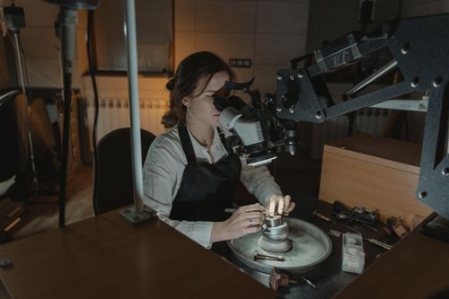 Free A woman jeweler crafting intricate pieces with precision under a microscope in a workshop. Stock Photo