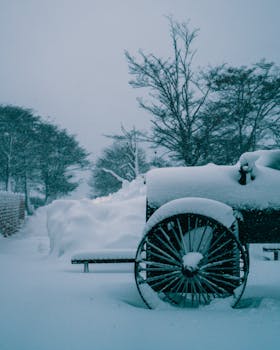 A rustic wagon blanketed in snow during a serene winter day, surrounded by snowy trees.