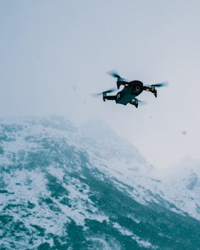 A drone flying high above snow-covered mountains in a serene winter setting.
