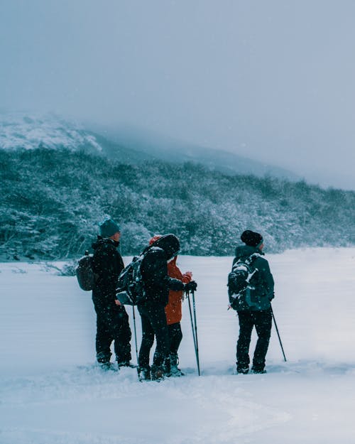 3 Pessoas Com Jaqueta Preta E Calça Vermelha Em Pé No Solo Coberto De Neve