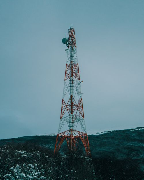 Free A steel communication tower stands tall against a snowy mountain backdrop in winter. Stock Photo