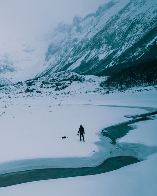 A lone trekker stands amidst a snowy mountain landscape, capturing the essence of remote adventure.