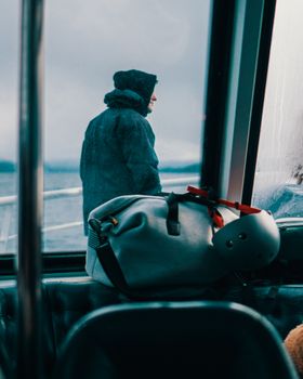Caught in a contemplative moment, a hooded man gazes at the ocean from inside a ferry.
