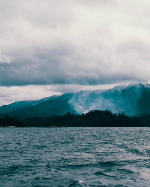 Body of Water Near Mountain Under Cloudy Sky