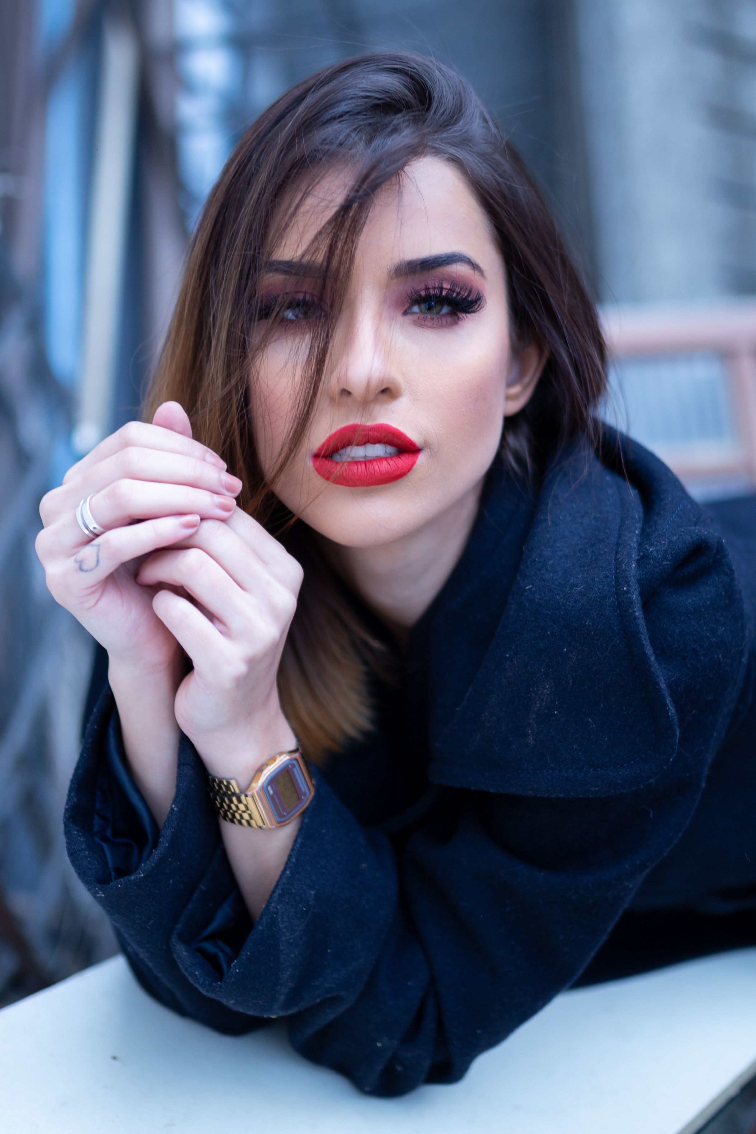 Stylish woman with red lipstick posing outdoors in a black coat. Perfect for fashion and lifestyle themes.