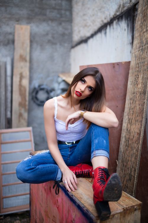 Free Trendy woman sitting on wooden crate, showcasing street fashion in casual outfit. Stock Photo