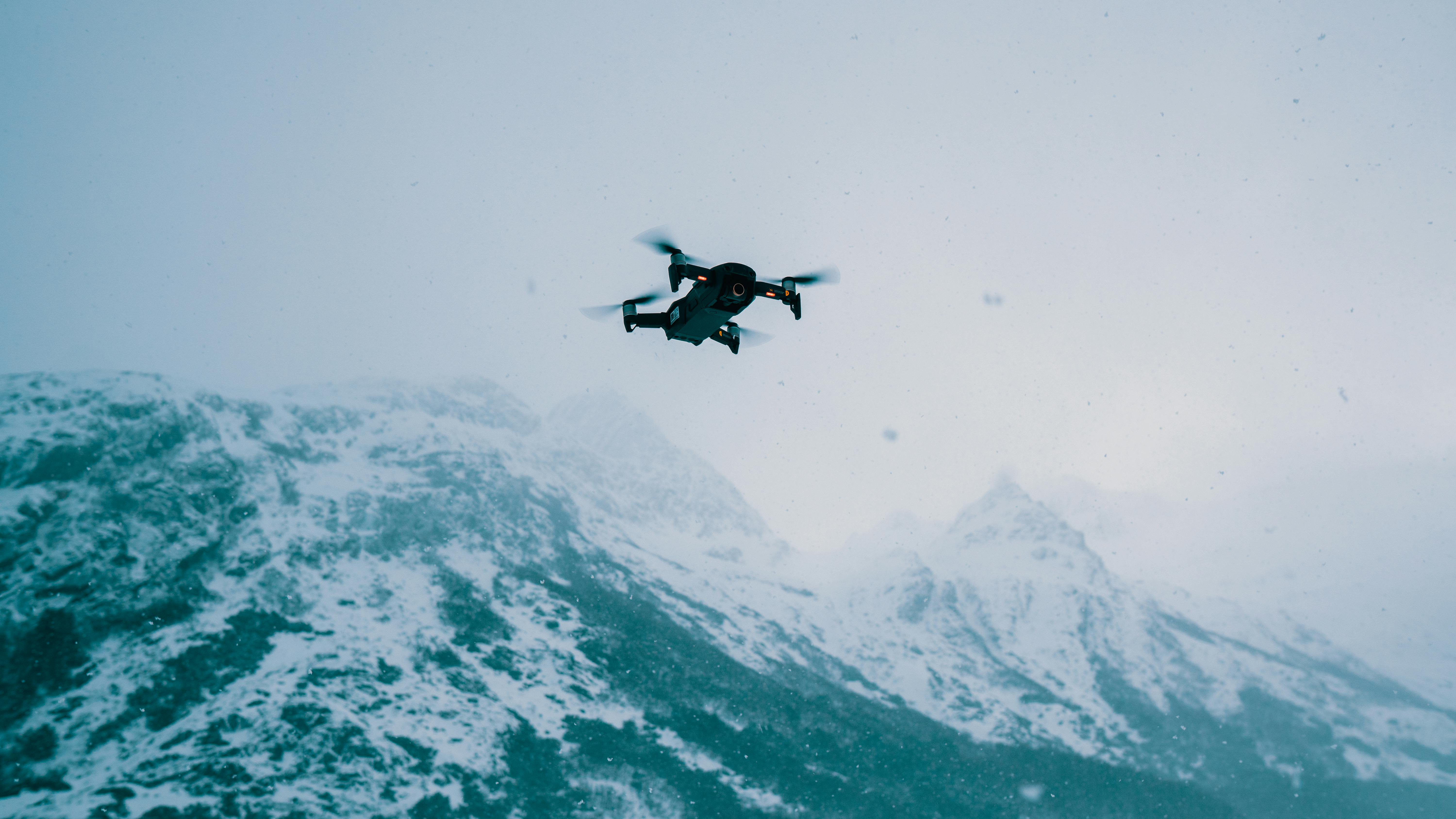 A drone flies over a vast snow-covered mountain range during wintertime.
