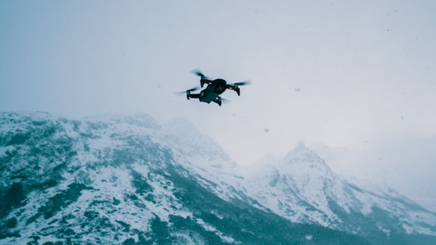 A drone flies over a vast snow-covered mountain range during wintertime.