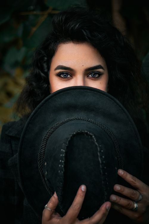 Free Close-up portrait of a woman holding a fedora, emphasizing her striking eyes. Stock Photo