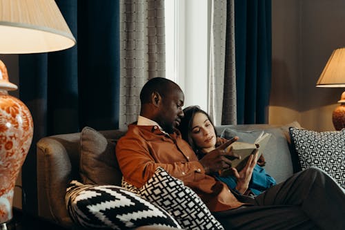 Man and Woman Sitting on Couch while Reading a Book