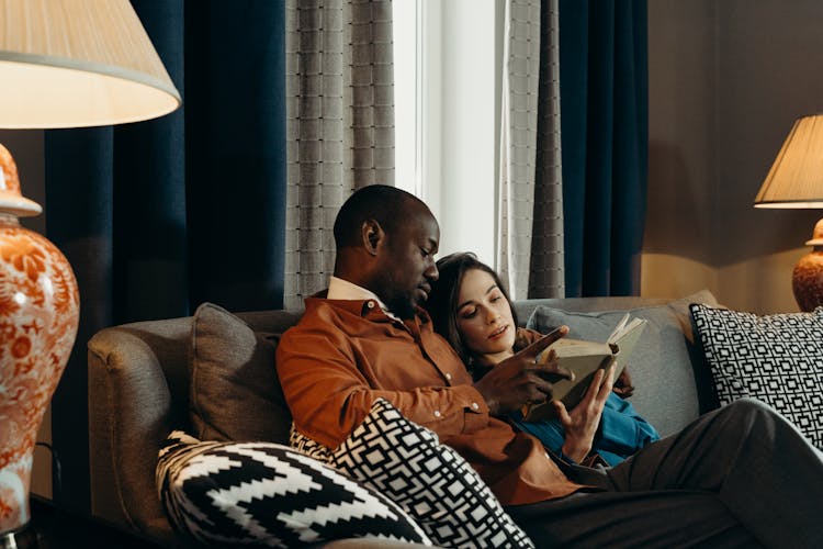 Man And Woman Sitting On Couch While Reading A Book